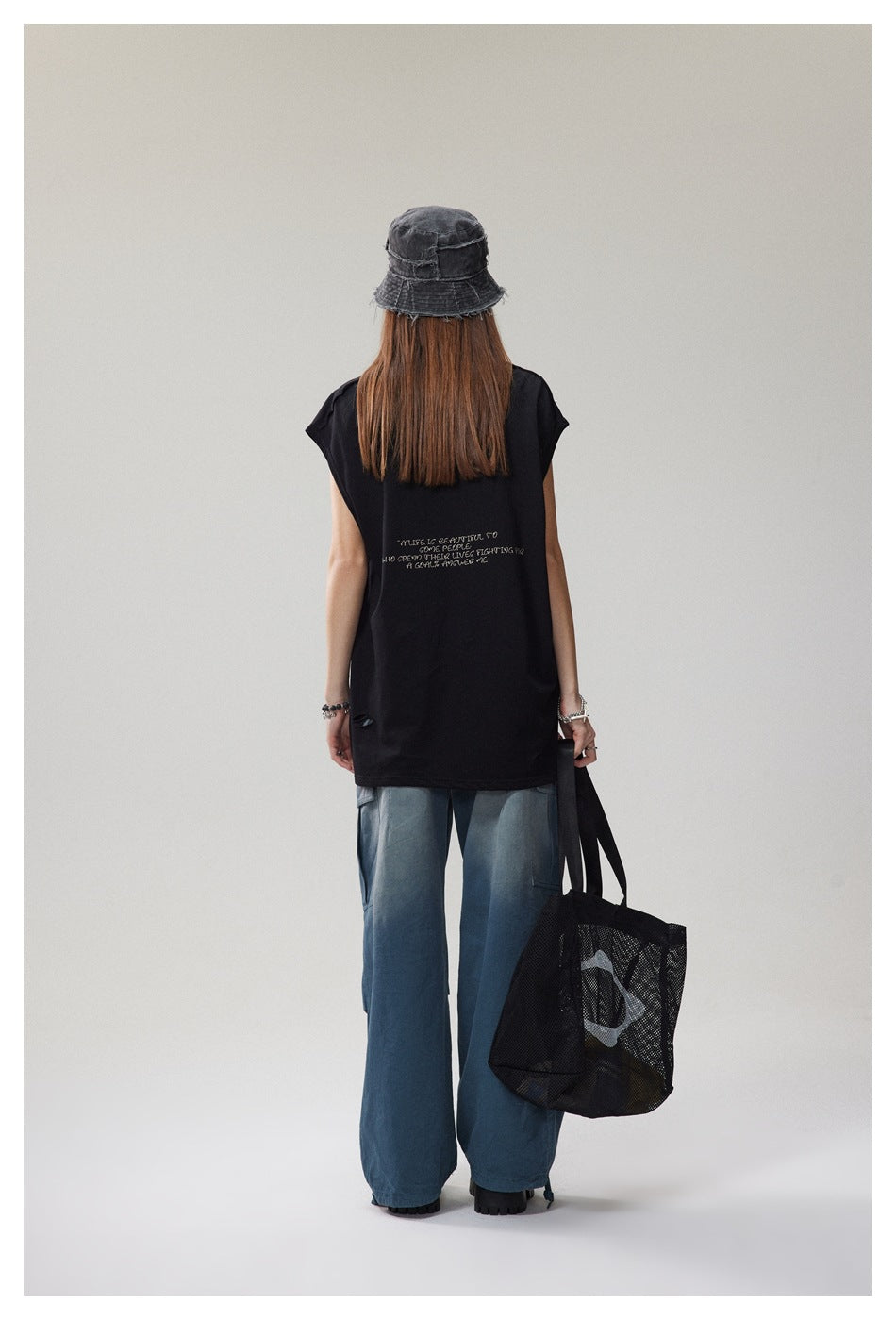 Back view of a model wearing a loose black cap-sleeve T-shirt with a small English quote printed between the shoulders.