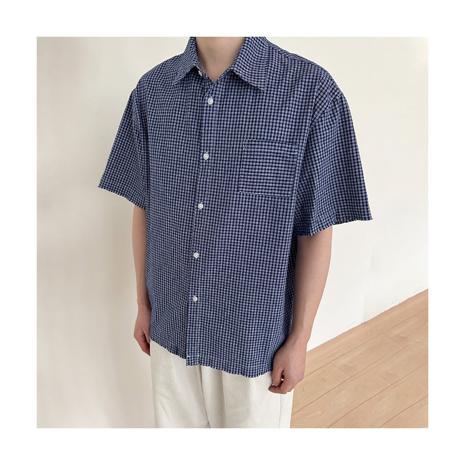 Person wearing a blue gingham short-sleeve shirt buttoned up, with frayed sleeve edges, paired with white pants