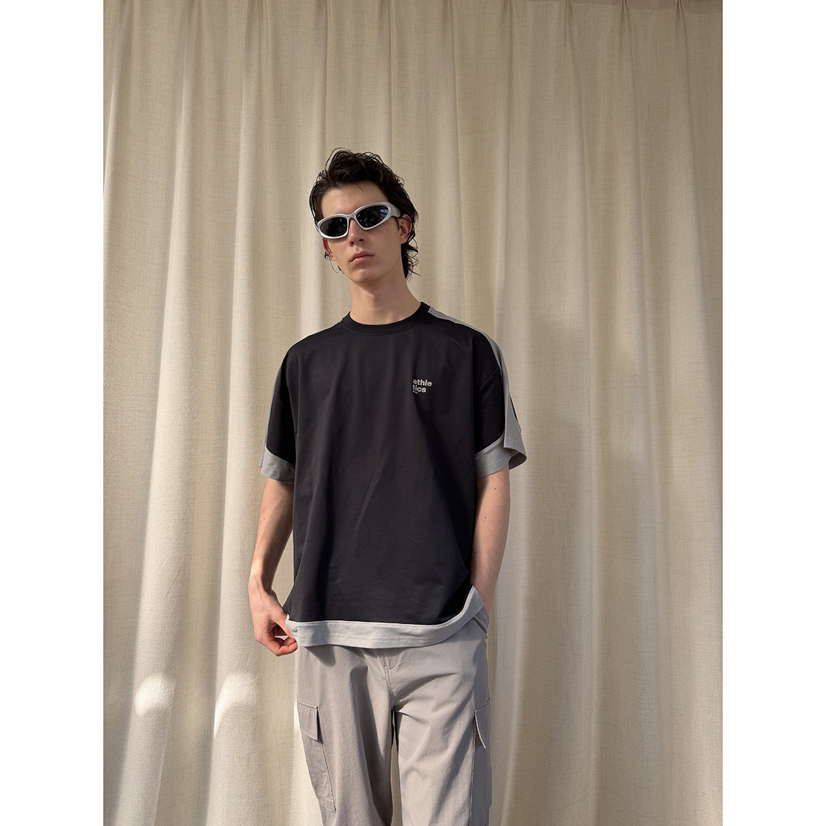 Model wearing a black T-shirt with gray contrast sleeves and hem; the shirt is shown from the front.