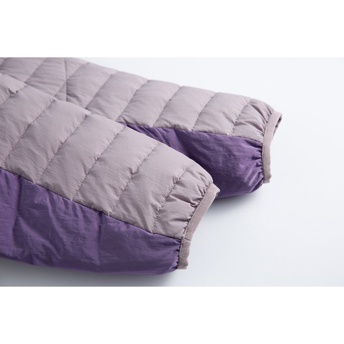 Close-up of quilted jacket sleeves with lavender-gray panels, deep purple sections and ribbed cuffs.