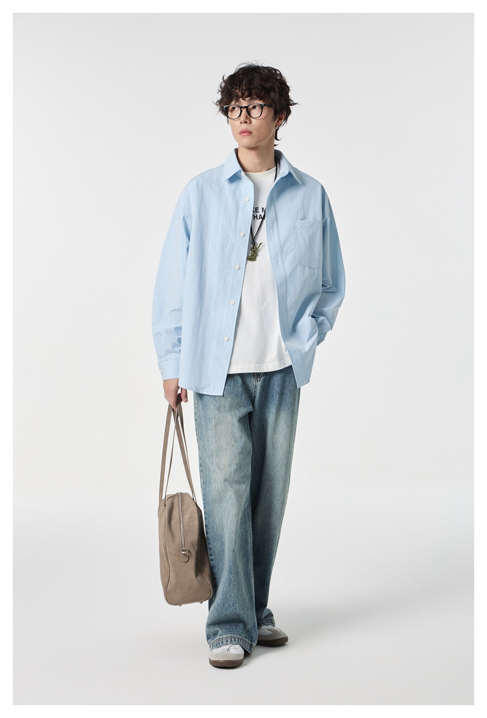 Model wearing an open pale blue button-up shirt over a white graphic tee and loose blue jeans.