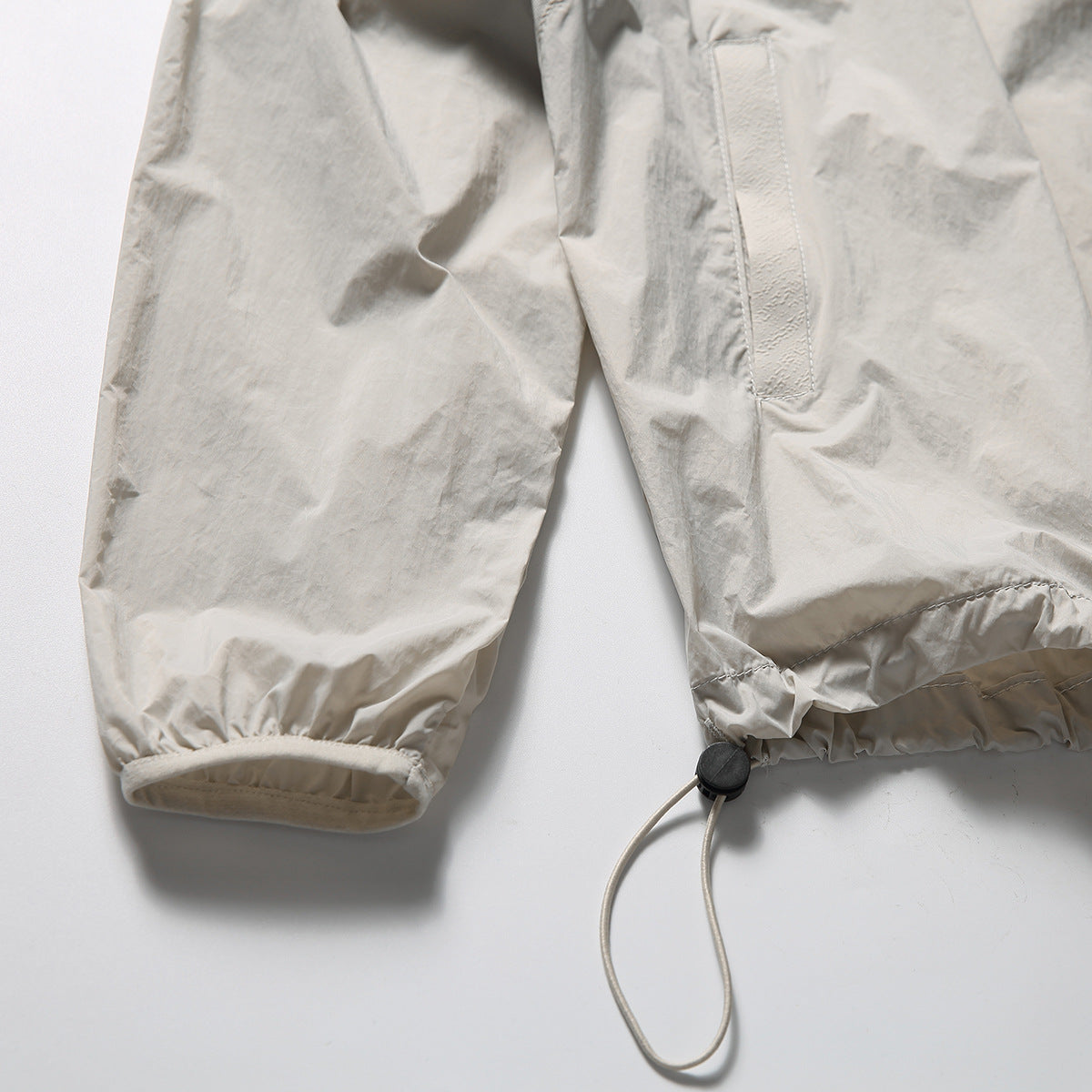 Close-up of a light beige jacket sleeve cuff and lower hem with an elastic drawcord and toggle.