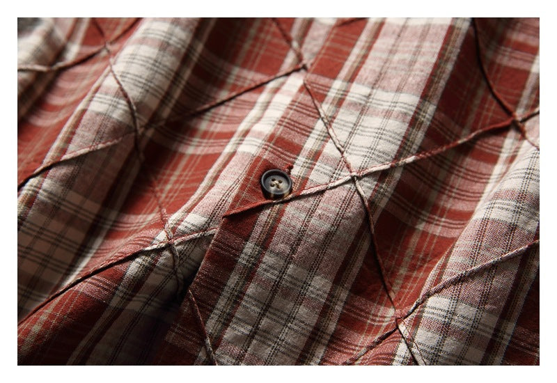 Close-up of a dark button and overlapping plaid fabric panels on the shirt.