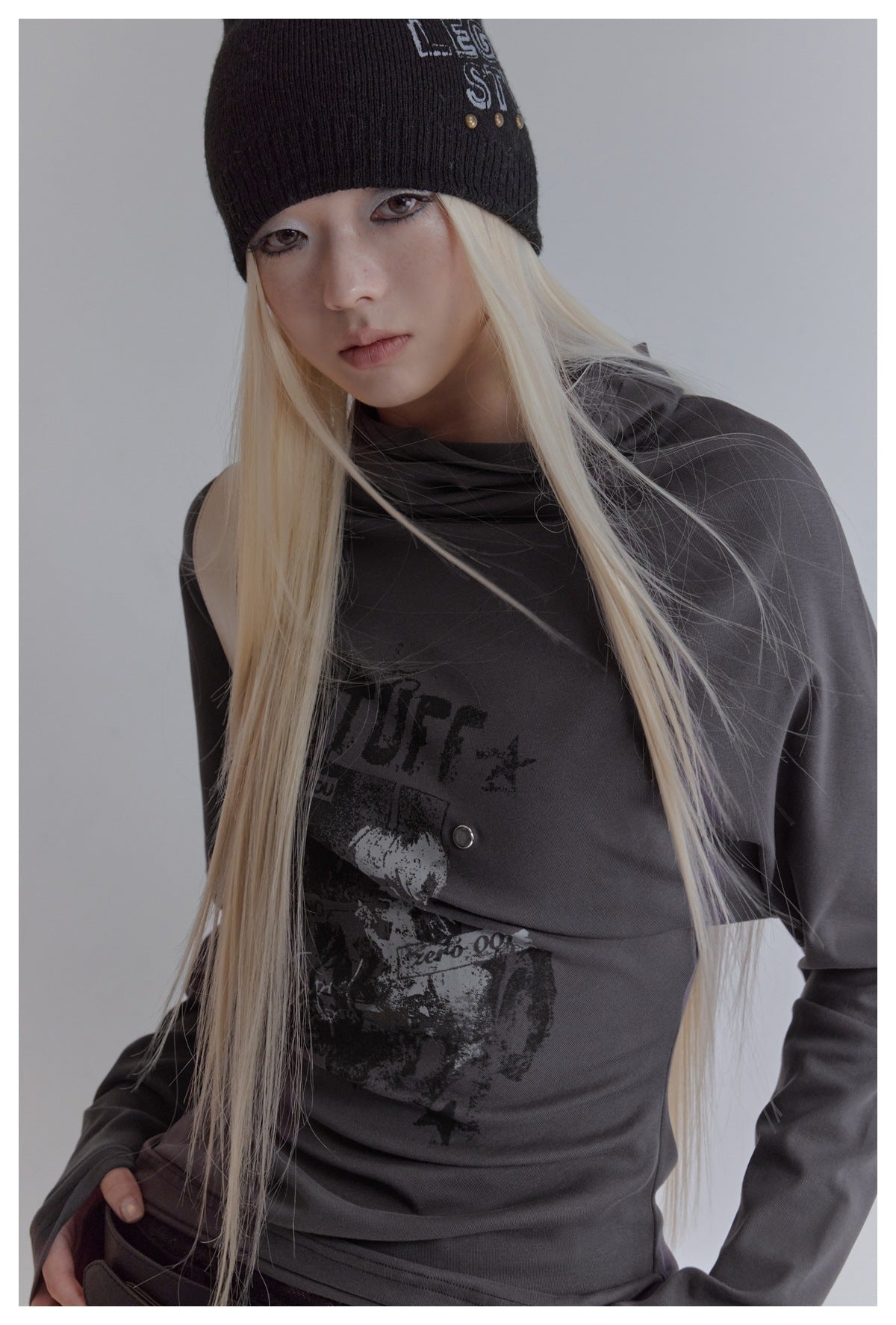 Close-up of model in dark gray high-neck graphic top with black knit beanie and long blonde hair