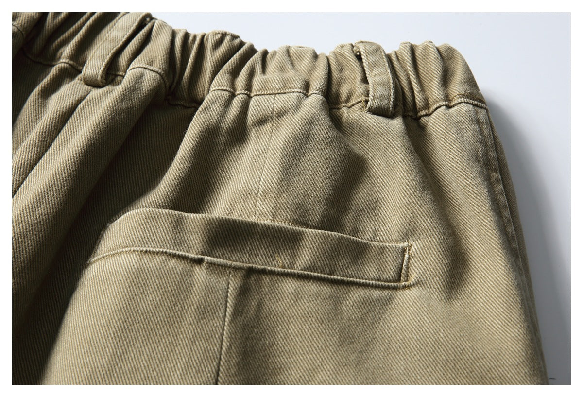 Close-up of khaki trousers showing an elastic waistband, belt loops, and a welt pocket.