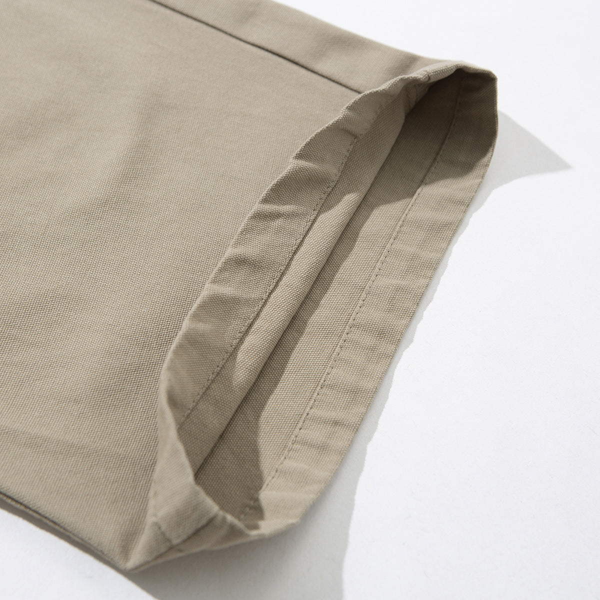 Close-up of the wide stitched hem and textured fabric of beige pants.