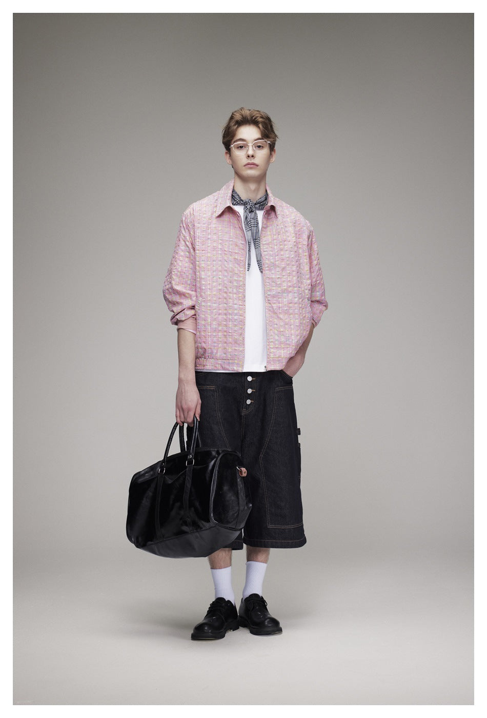 Full-length model wearing a pink plaid jacket and dark denim shorts, carrying a black bag.