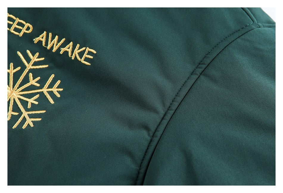 Close-up of a dark green jacket seam beside cropped gold snowflake embroidery and lettering.