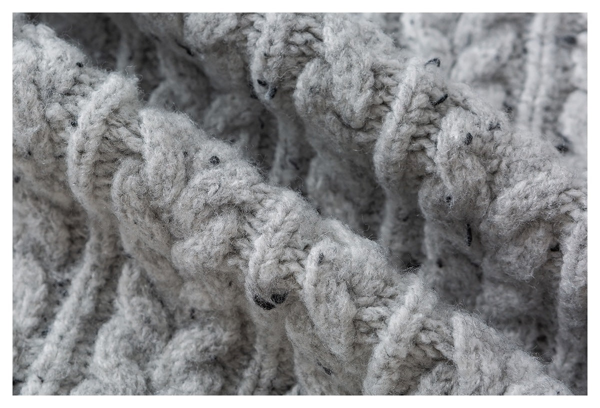 Macro view of chunky, looped light gray knit with scattered dark flecks and raised braided stitches.