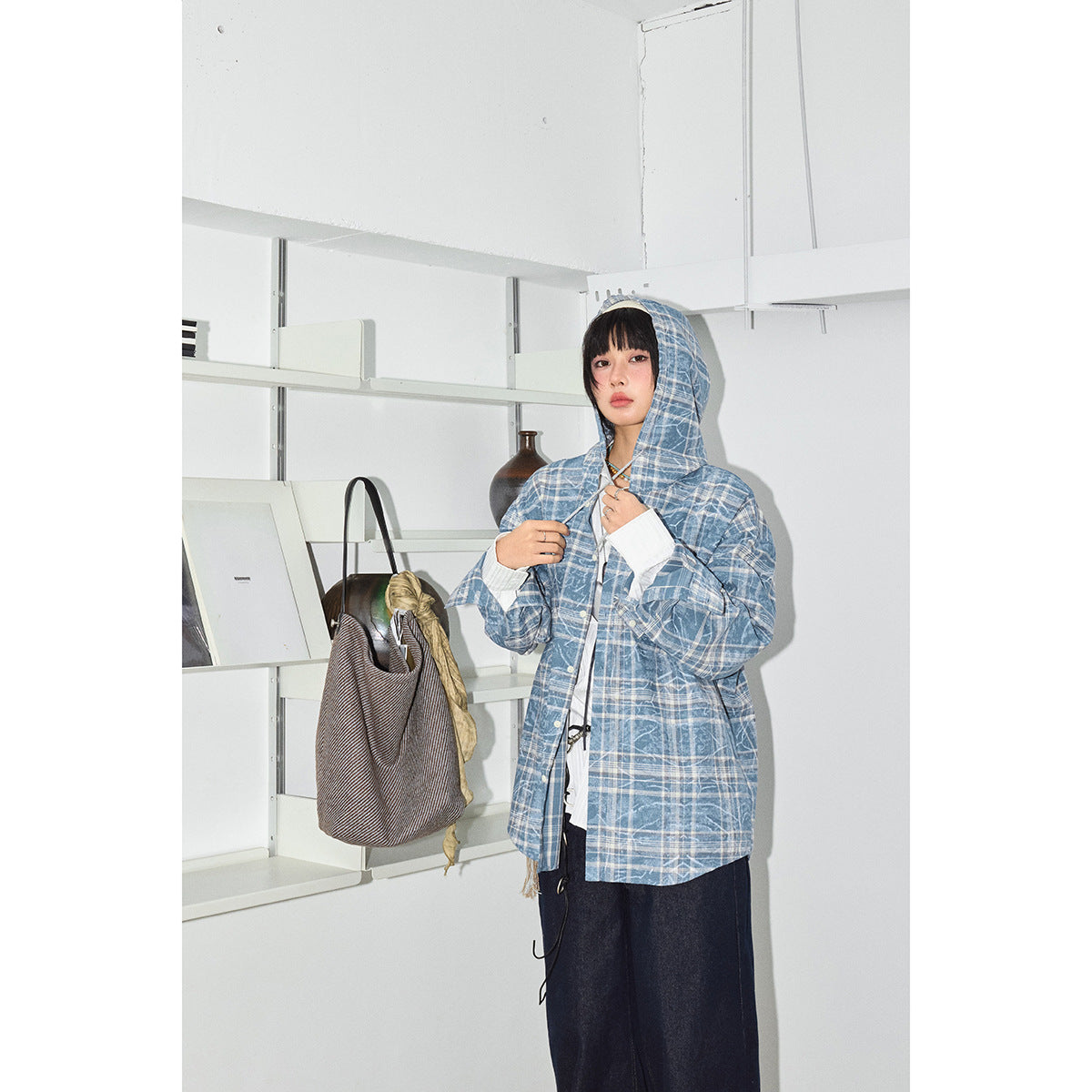 Model wearing the blue-and-white plaid jacket with its hood up, over a white blouse and dark wide-leg jeans.