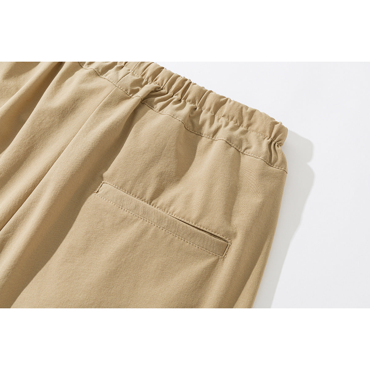 Close-up of tan trousers showing the gathered elastic waistband and a single back welt pocket.