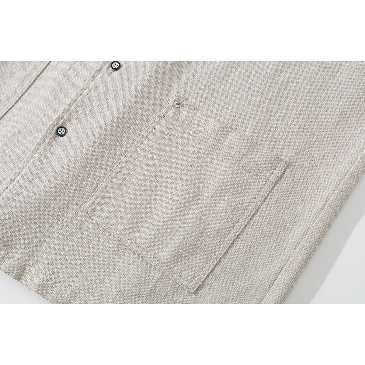 Close-up of the light beige shirt's button front and single rectangular chest pocket.