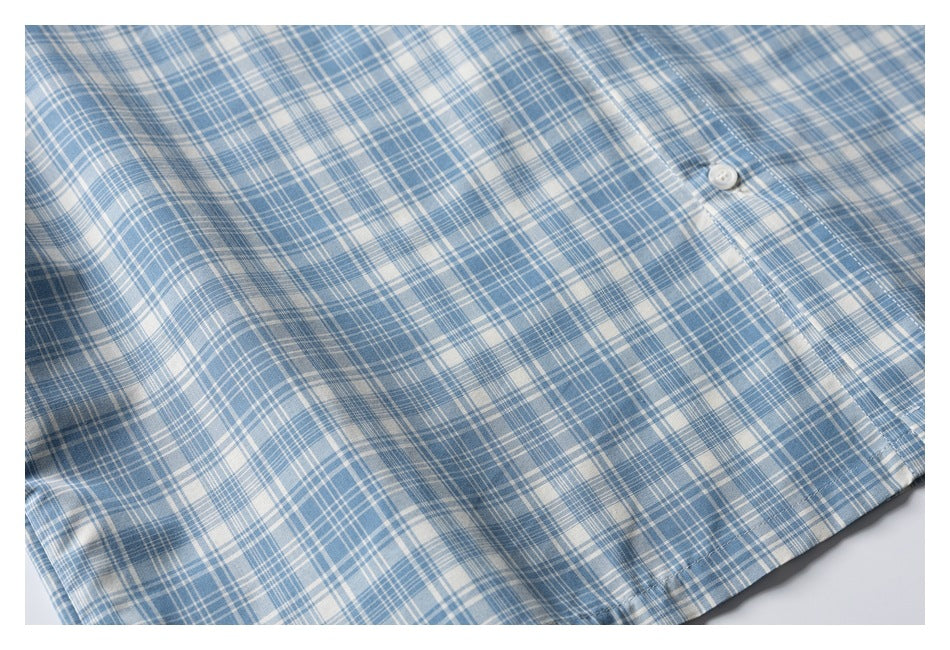 Partial flat-lay front of a blue-and-white plaid shirt, showing a button and lower hem.