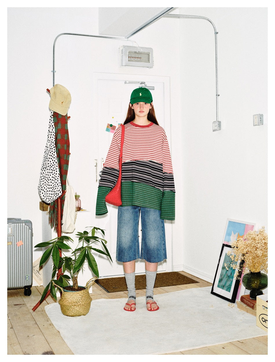 Model wearing an oversized striped patchwork long-sleeve top with denim shorts, green cap and red bag, facing front