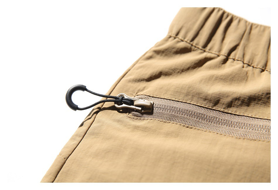 Close-up of a tan shorts pocket zipper with a black cord loop pull.