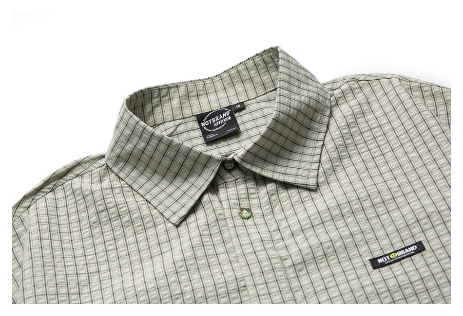 Cropped front view of a pale gray-green plaid button-up shirt with a pointed collar and black chest patch.