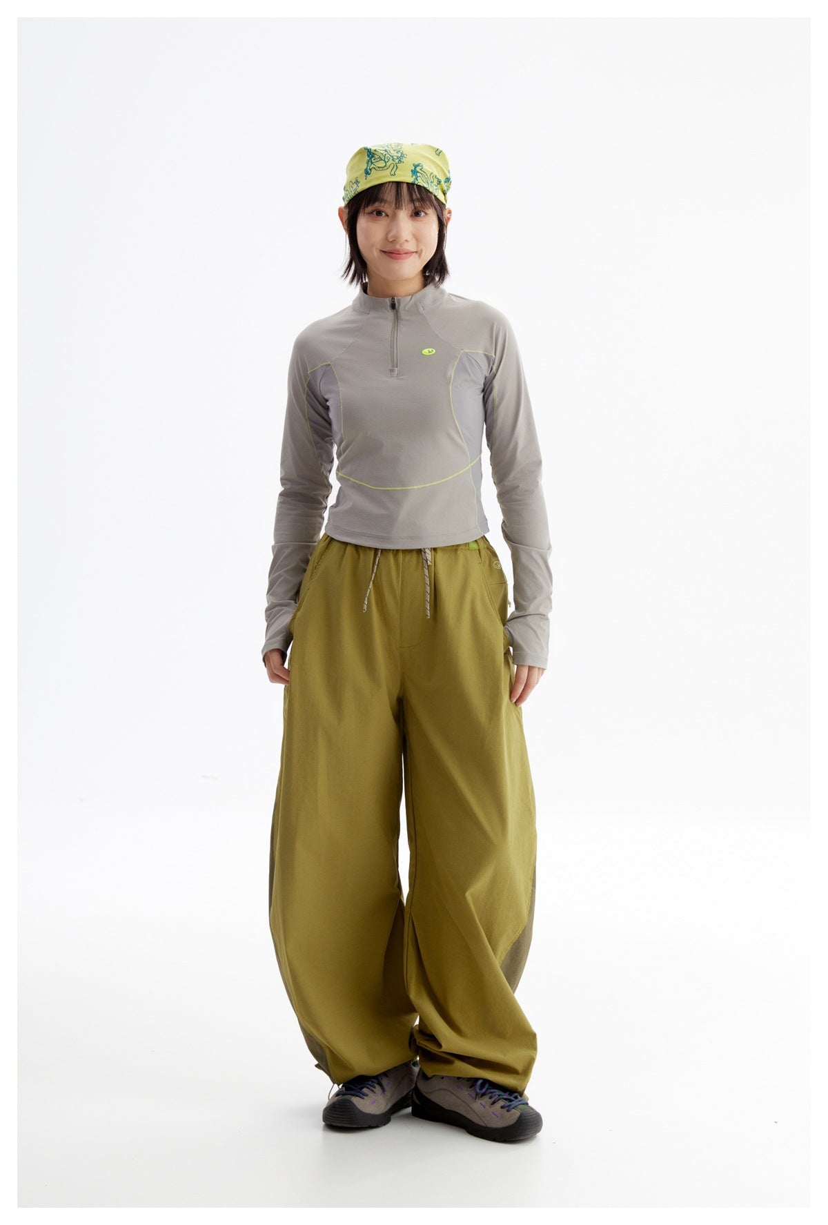 Model wearing a gray long-sleeve quarter-zip top with lime piping, olive wide-leg pants, and a yellow-green patterned