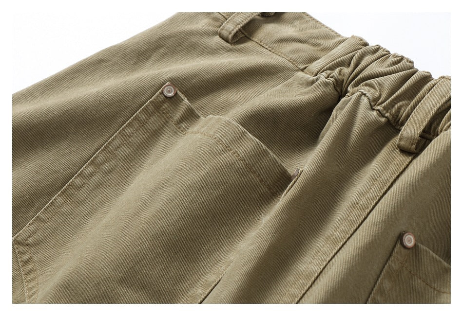 Close-up of khaki trousers showing a large patch pocket, metal rivets and a gathered elastic waistband.