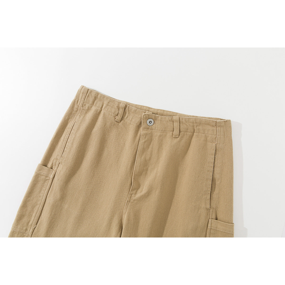 Close-up of the upper front of tan utility trousers, showing the waistband, button, fly seam and side pockets.