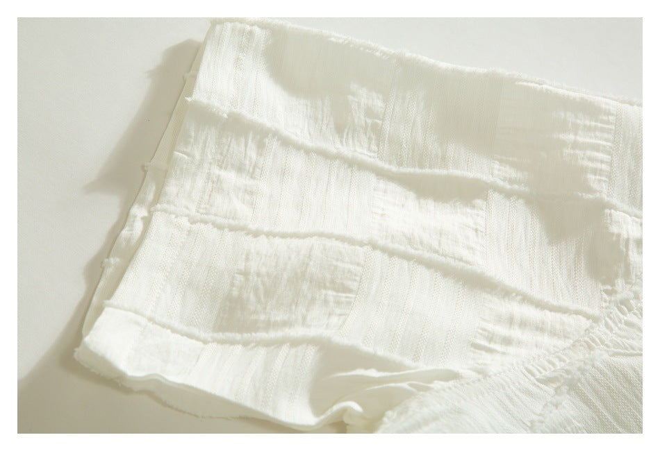Close-up of an ivory garment edge with textured panels, stitched seams, and a softly frayed hem.