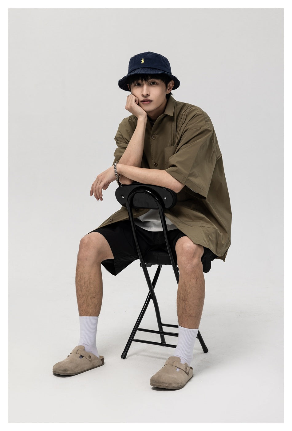 Closer front view of a seated model wearing an olive short-sleeve button-up shirt and black shorts.