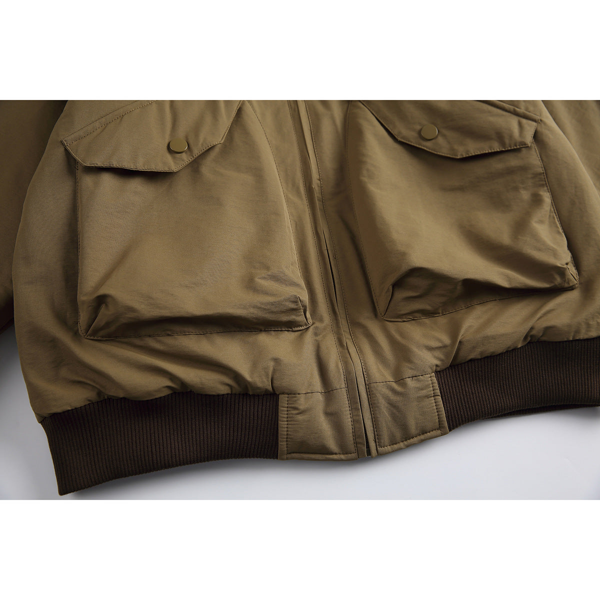 Close-up of a khaki bomber jacket’s two flap pockets, front zipper, and dark ribbed hem.