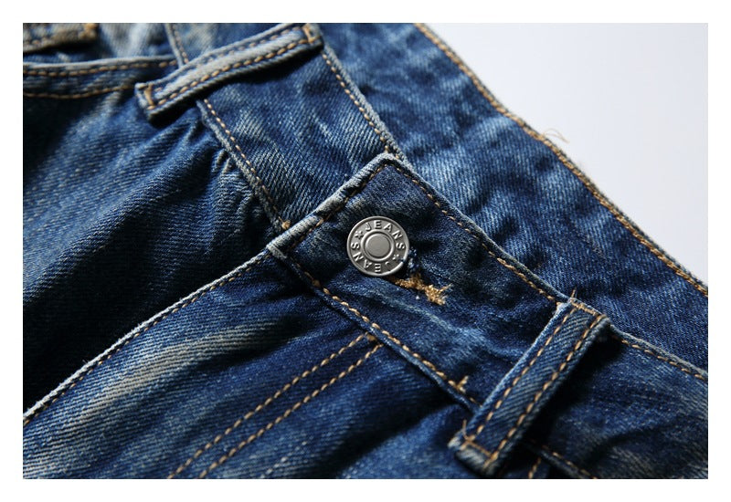 Close-up of blue jeans showing a metal waistband button, belt loop, and contrast stitching.