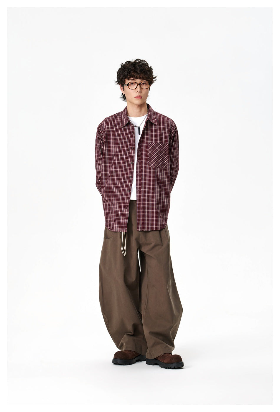 Full-length model wearing a burgundy check button-up shirt and loose brown trousers.