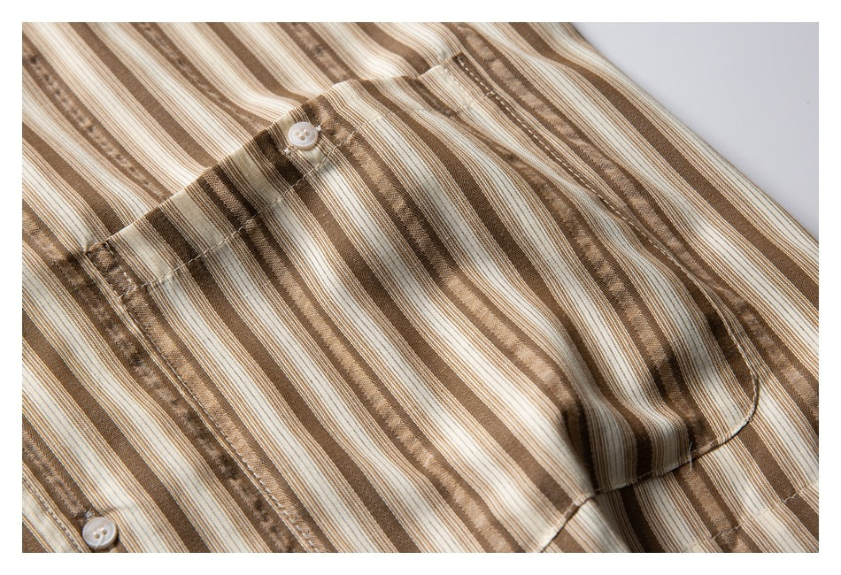 Close-up of a chest pocket and white button on the cream, tan, and brown striped shirt.
