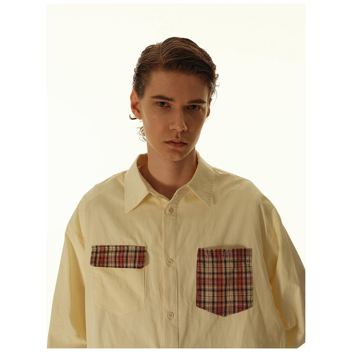 Close view of a model wearing a cream button-up shirt with two contrasting plaid chest pockets.