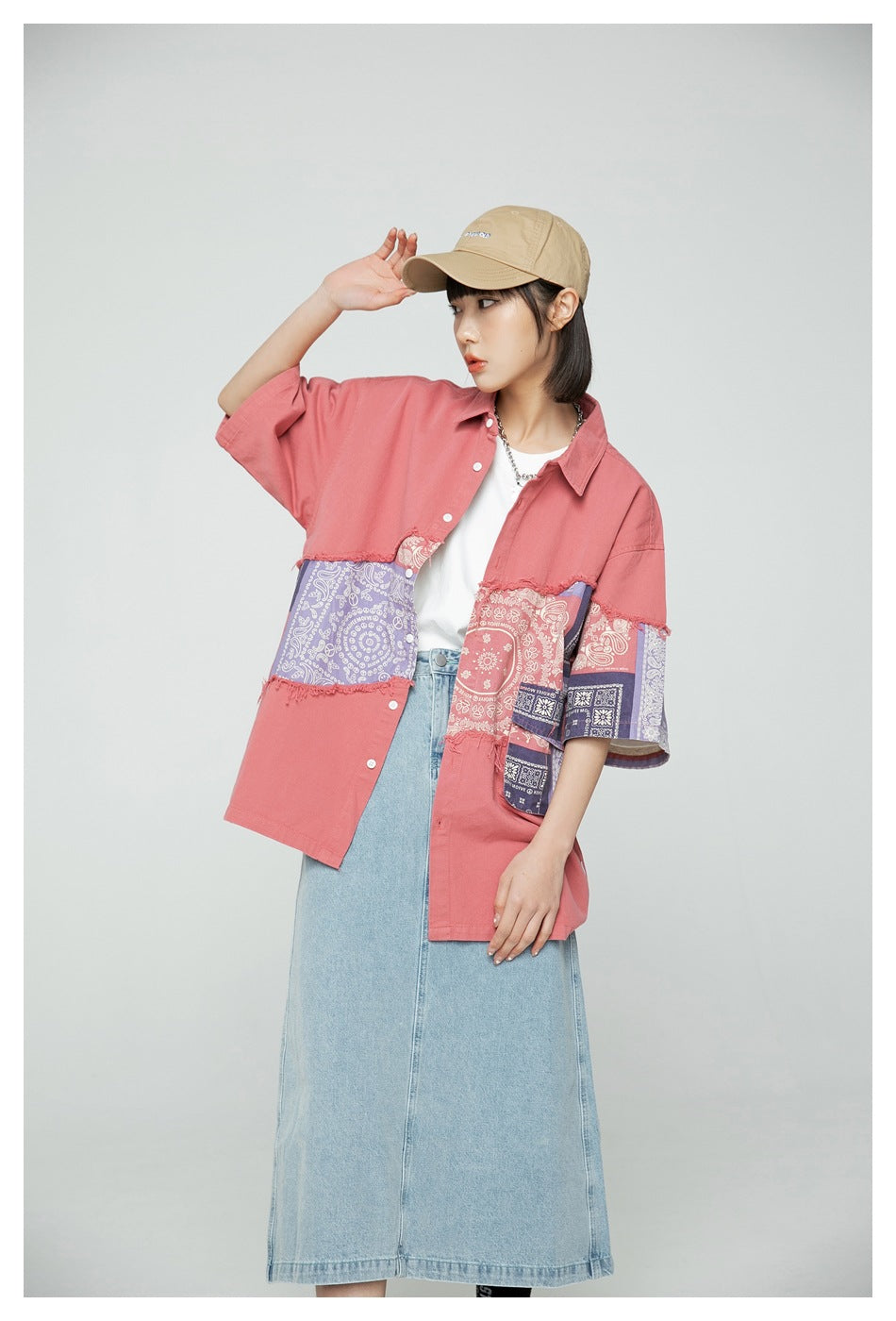 Model wearing a coral oversized shirt with contrasting paisley patchwork panels, shown from the front at an angle.