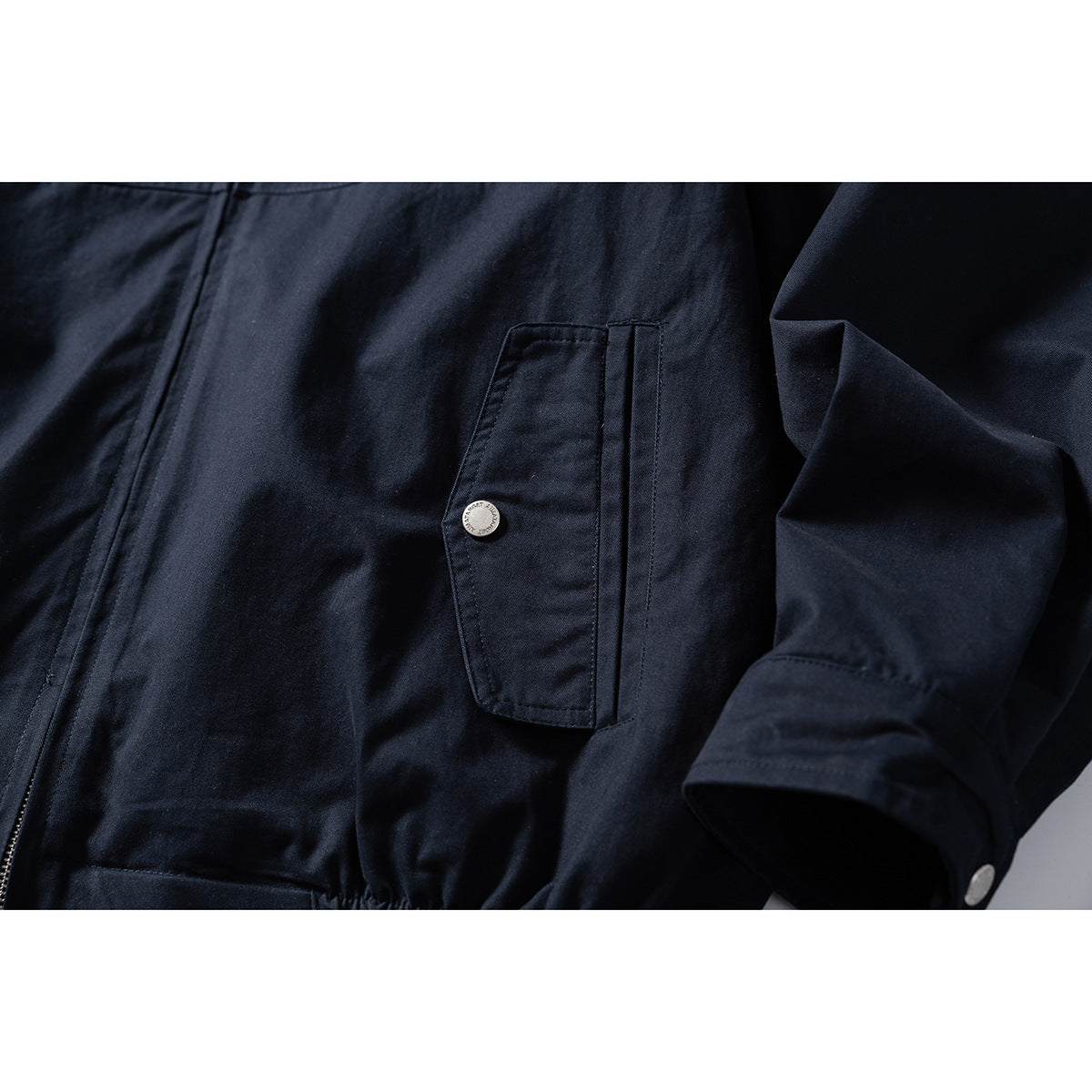 Close-up of a navy jacket's flap pocket with a metal snap and sleeve cuff.