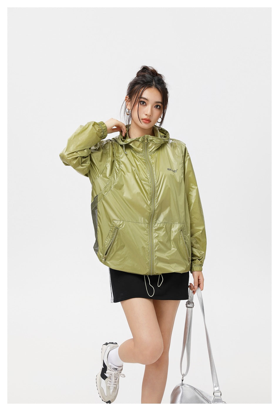 Model wearing an olive green hooded zip jacket with side mesh panel and zip pockets, three-quarter view with silver bag