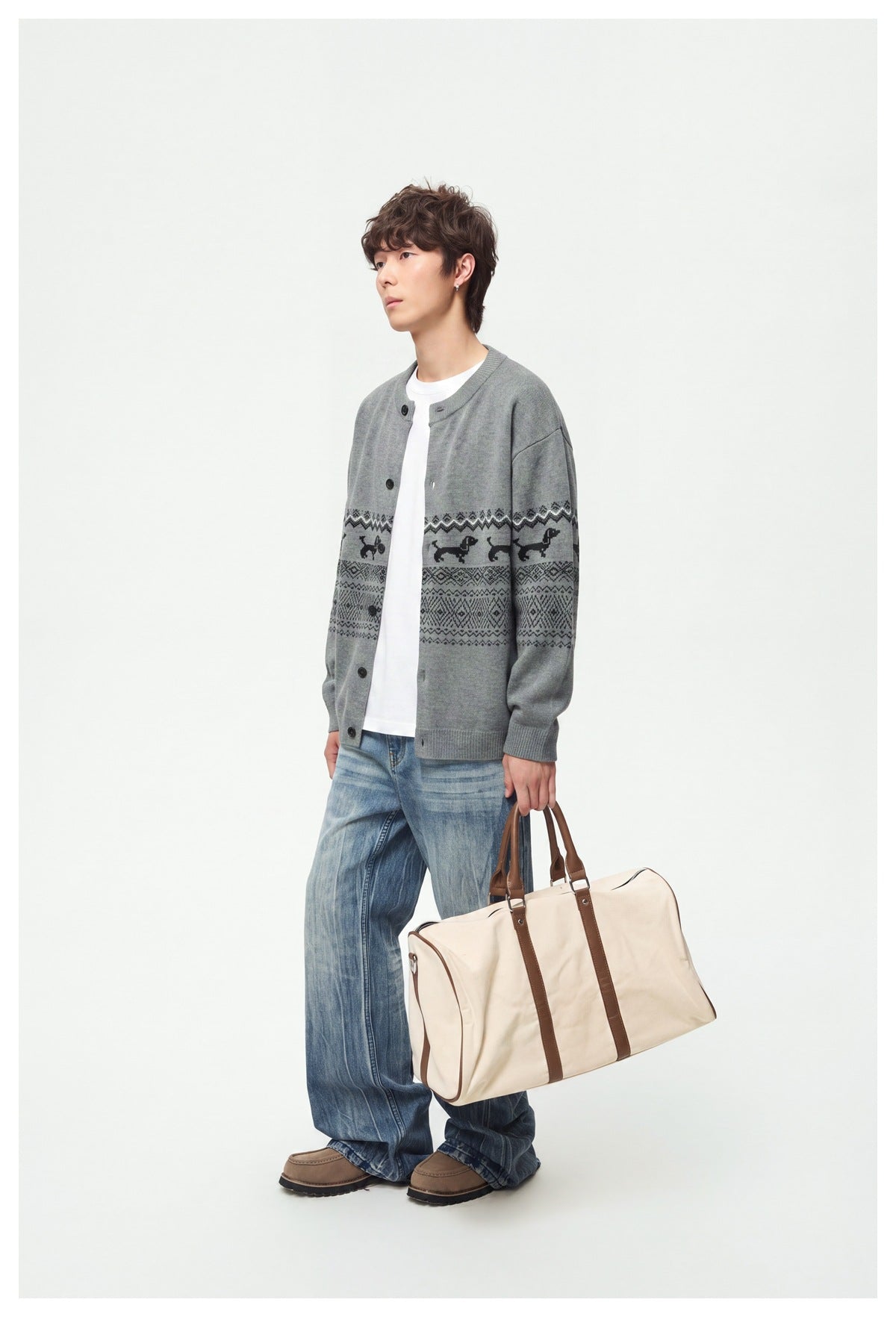 Full-length side view of model in gray patterned cardigan, white tee and wide jeans carrying a duffel bag
