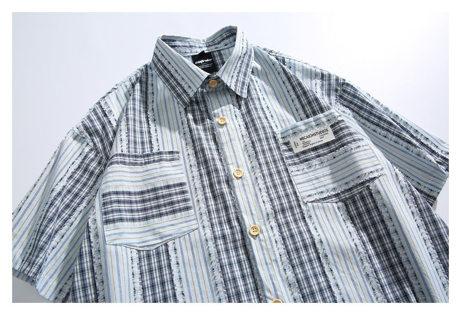 Front view of a short-sleeve button-up shirt with blue, gray, and white striped plaid panels and two chest pockets.