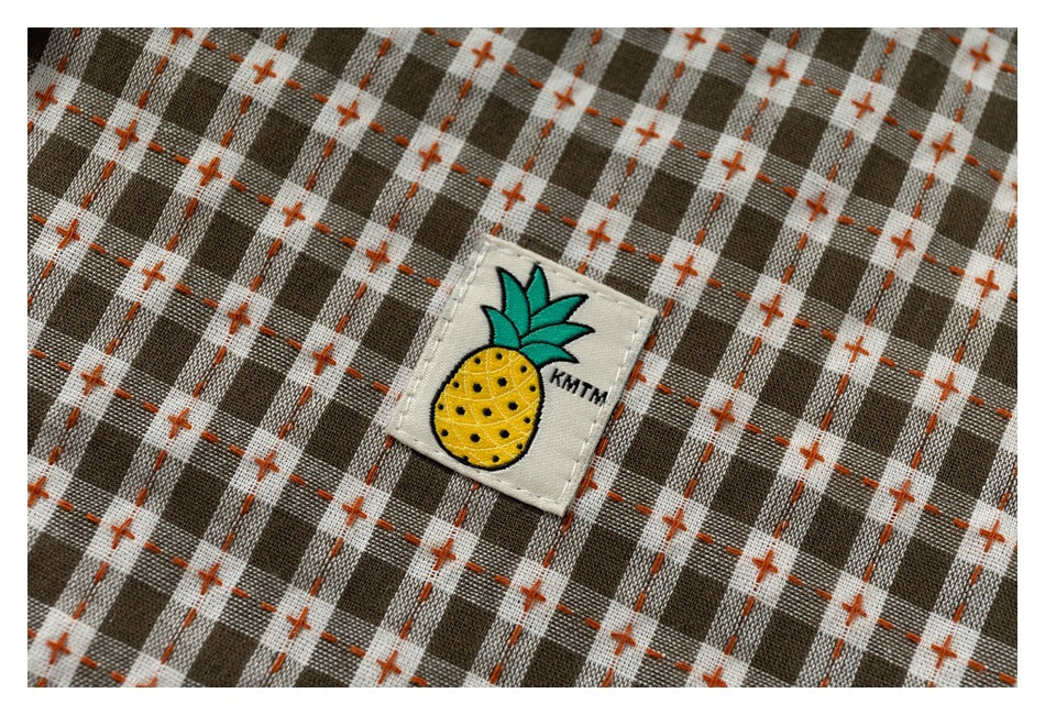 Close-up of a sewn pineapple patch on brown-and-cream checked fabric with orange cross-stitch accents.