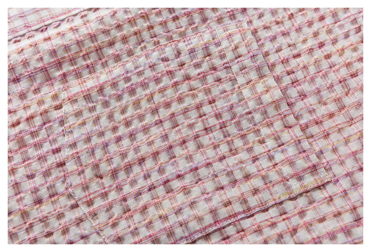 Close-up of cream plaid fabric showing intersecting pink and muted yellow lines with several stitched seams.