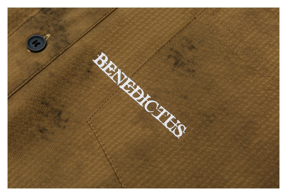 Close-up of white “BENEDICTS” lettering on the brown textured shirt beside a dark button.