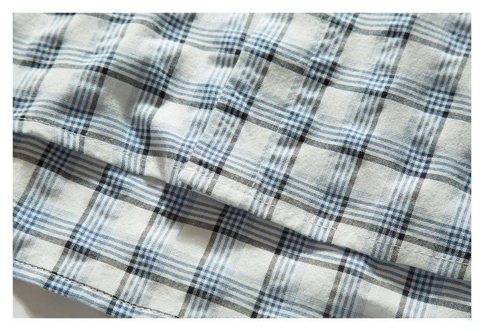 Close-up of white fabric with blue and charcoal plaid, showing a folded stitched edge.
