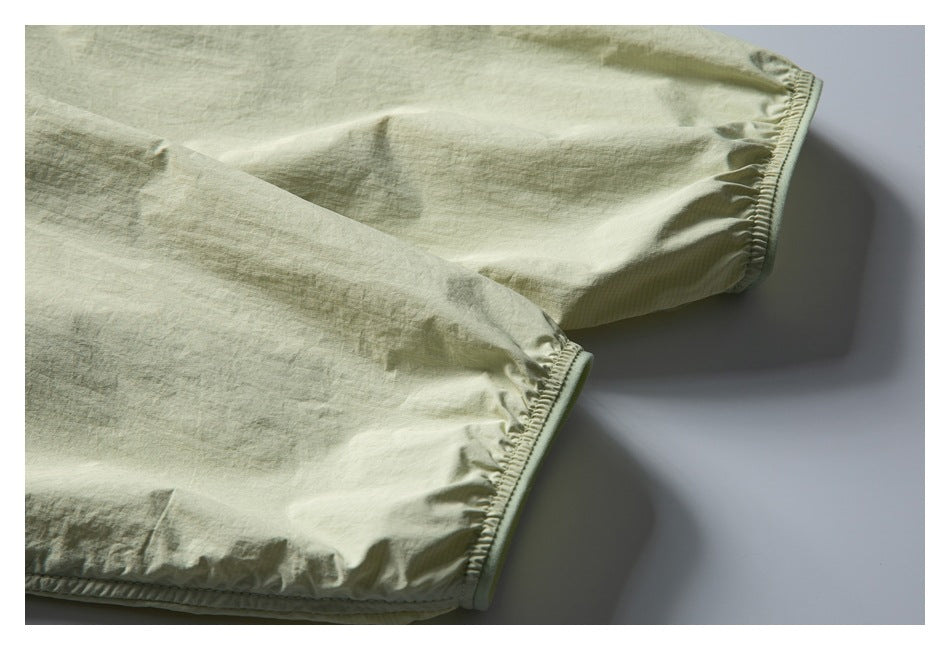 Close-up of two gathered, elasticized edges on a pale sage garment.