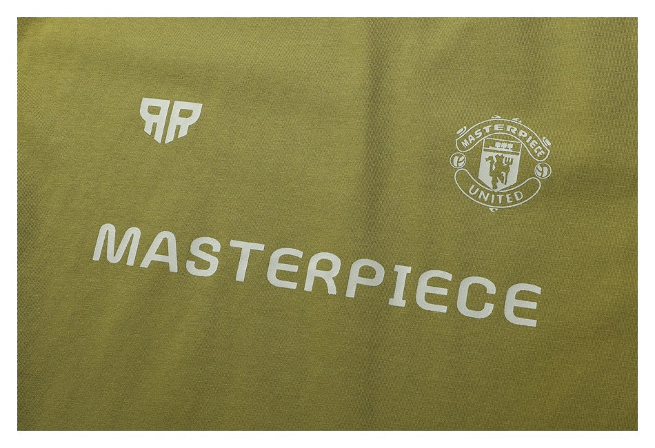 Close-up of white shirt print on olive fabric, including a crest, a monogram, and the word “MASTERPIECE.”