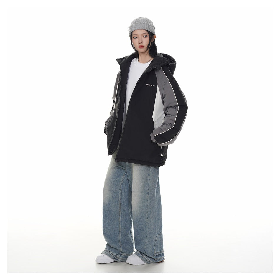Model wearing a black hooded jacket with gray and white panels, shown with loose blue jeans.