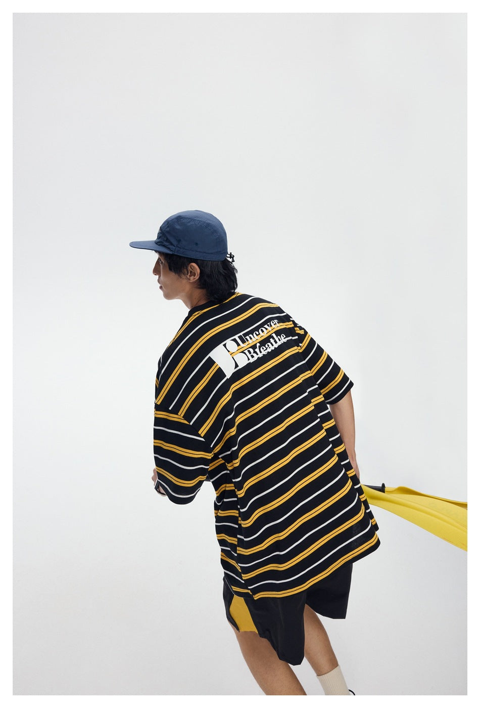 Angled rear view of a model in a black, yellow, and white striped T-shirt with a large white back print.