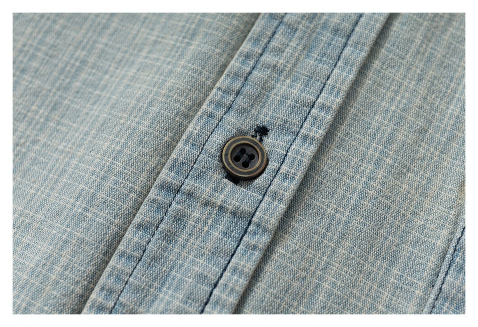Close-up of a dark button on the placket of a light blue and cream woven shirt.