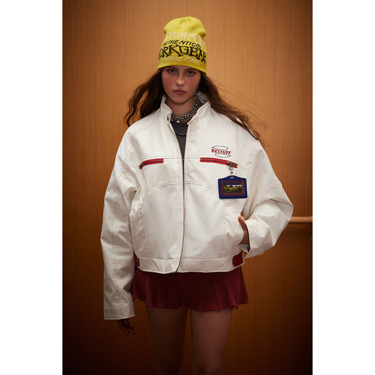 Model wearing a white zip-front jacket with red zipper details and a yellow printed beanie.