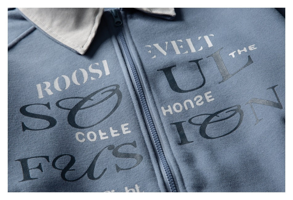 Close-up of a blue zip-up garment with a light collar and large contrasting English lettering.