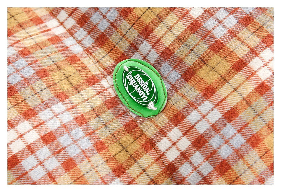 Close-up of a small green oval patch on the orange, cream, and tan plaid jacket.