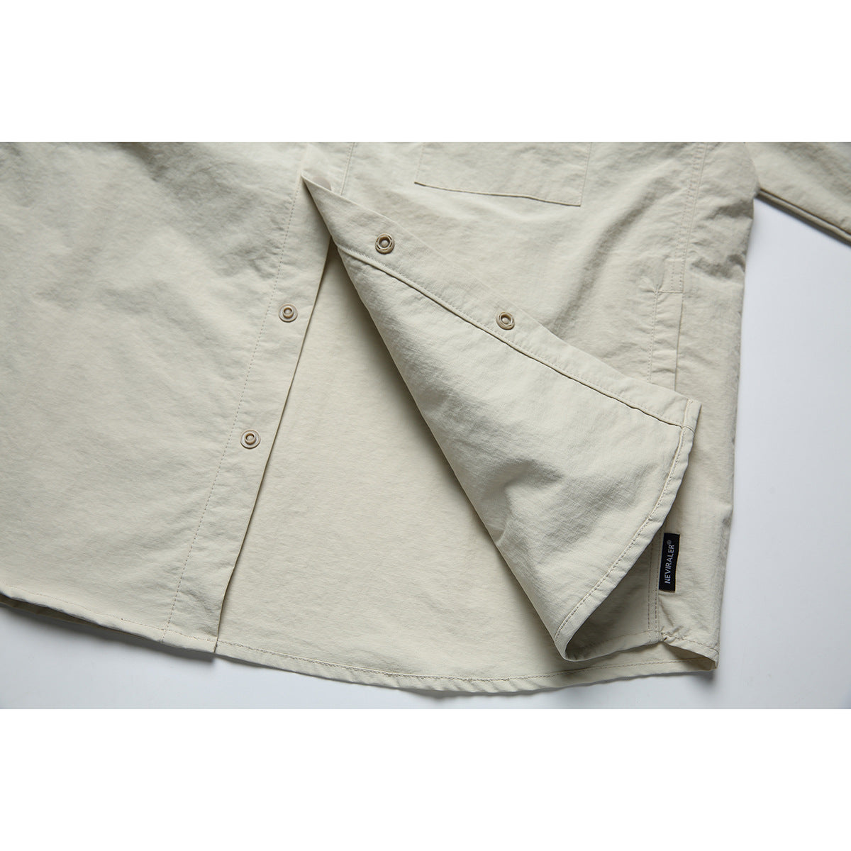 Close-up of the pale beige shirt jacket opened to show its inner snap placket and a small sewn-in label.