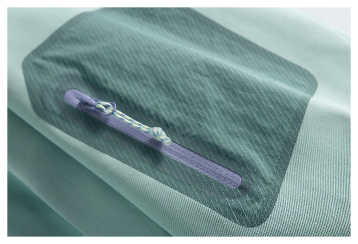 Close-up of a lilac zipper and patterned pull on a dark teal stitched panel of a mint garment.