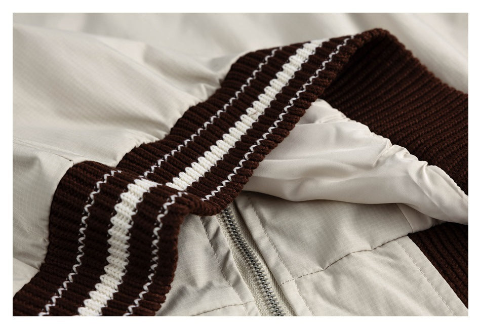 Close-up of the beige jacket's zipper and dark brown ribbed trim with white stripes.